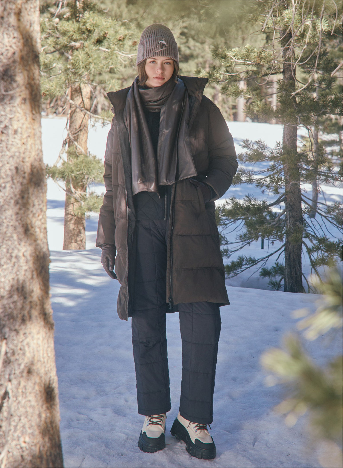 Alp N Rock dark brown long puffer ski coat, taupe ribbed beanie, black puffer ski pants, and dark brown faux leather scarf